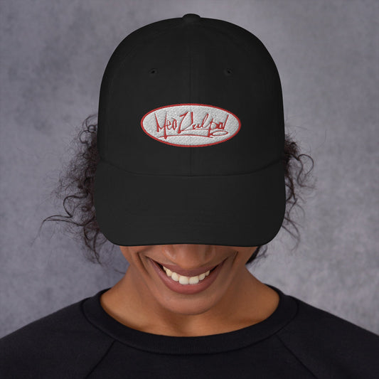 In a moment of quiet confidence, a girl tilts her head downward, her smile radiating positivity. A black hat, adorned with the red and white OG logo, stylishly covers her eyes. The logo, a symbol of her individuality, peeks out from beneath the hat's brim. The downward gaze, paired with the concealed eyes and the playful smile, creates an intriguing blend of mystery and charm. It's a snapshot of a person embracing their own uniqueness with a touch of understated confidence.